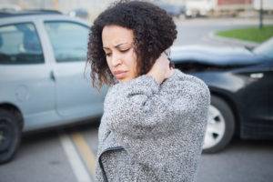 A woman rubs her neck at a car accident scene