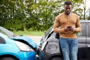 man on phone leans against wrecked car