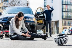 injured bicyclist holding knee in front of car and worried driver