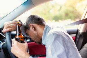 man slumped over steering wheel with beer bottle in hand